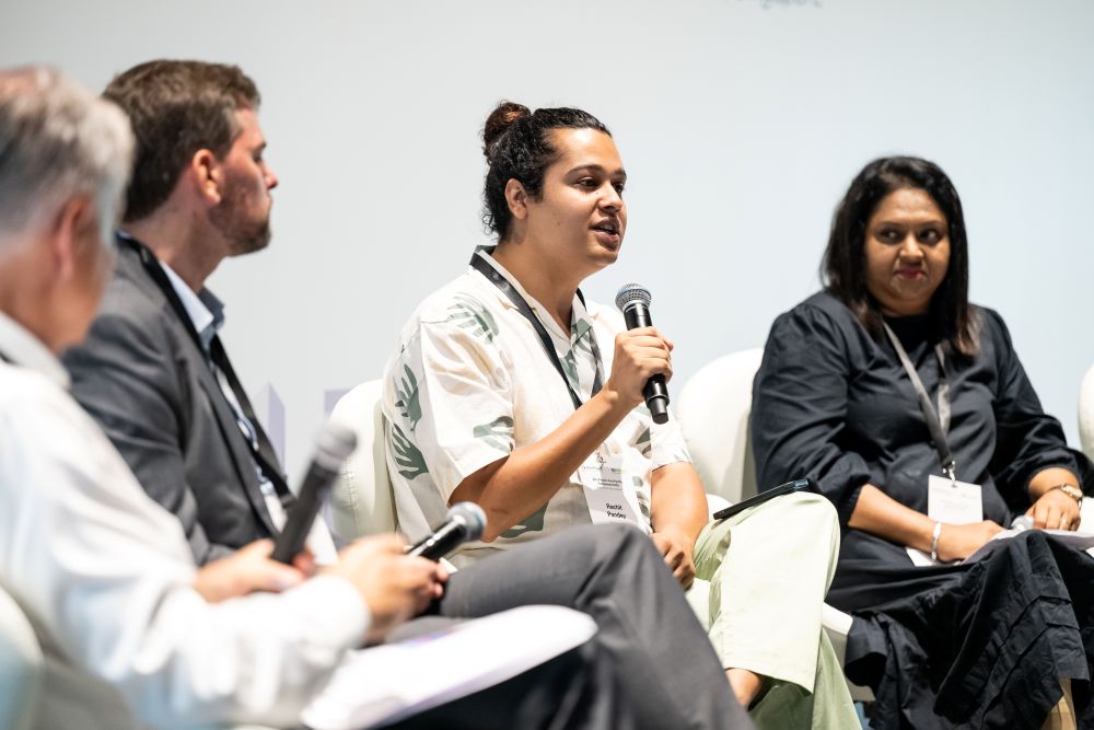 A man holding a microphone speaking on a panel while other panellists listen to him.